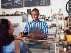 Young black male cafe owner handing drink off to customer over counter